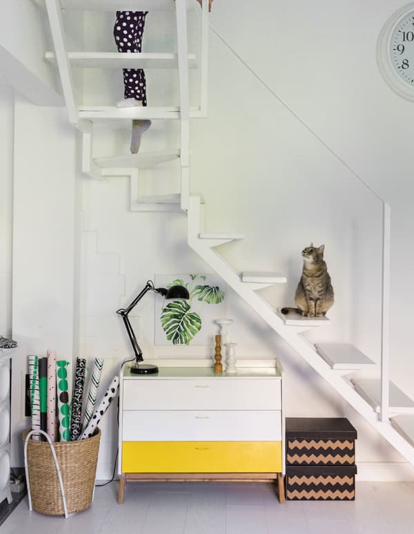 A white sideboard with a yellow drawer, under a white floating staircase.