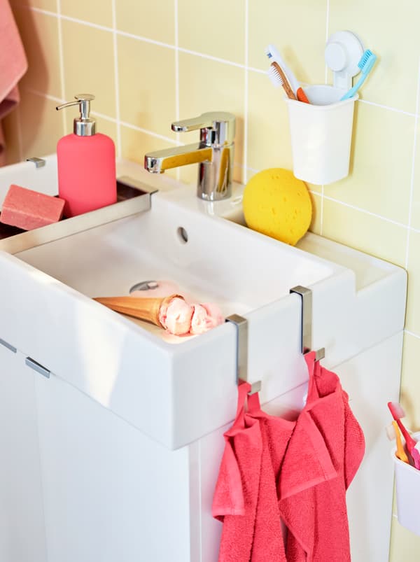 A white sink vanity with accessories and towels in coral and white. An ice cream is melting in the sink.