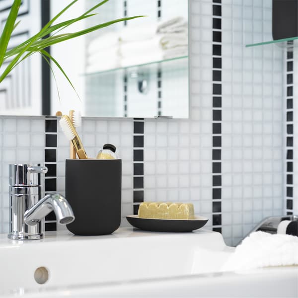 A white sink where toothbrushes stand in a dark grey toothbrush holder in a black/white bathroom. 