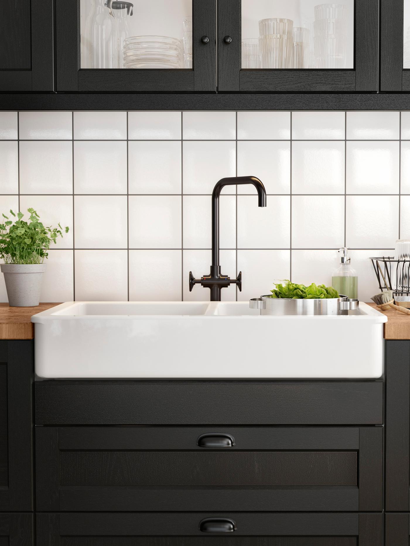 A white sink with a visible front and a black brushed metal mixer tap in a kitchen with stained black wood fronts.