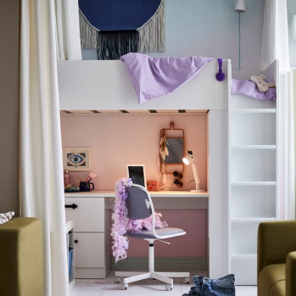 A white SMÅSTAD loft bed with desk that has an ÖRFJÄLL swivel chair in front of it with a feather boa draped over its back.