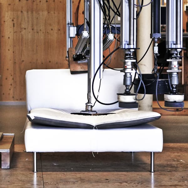 A white sofa undergoing a mechanical durability test with robotic equipment pressing on the cushions.