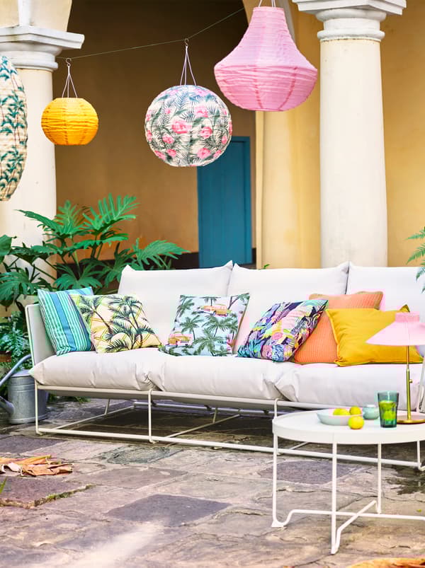 A white sofa with various colored and patterned scatter cushions placed outside with a variety of hanging lanterns.