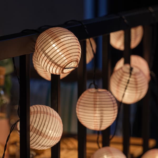 A white SOLVINDED LED lighting chain hung over a black balcony rail creating a cosy outdoor atmosphere. 