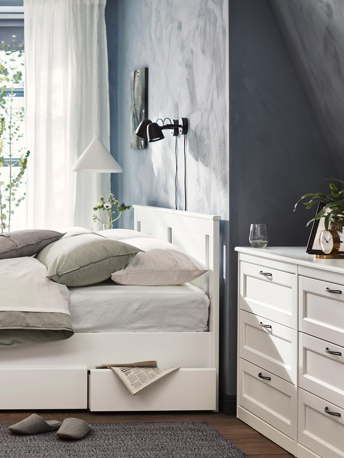 A white SONGESAND double bed with headboard in a light room with two under bed storage boxes, one of which is slightly open.