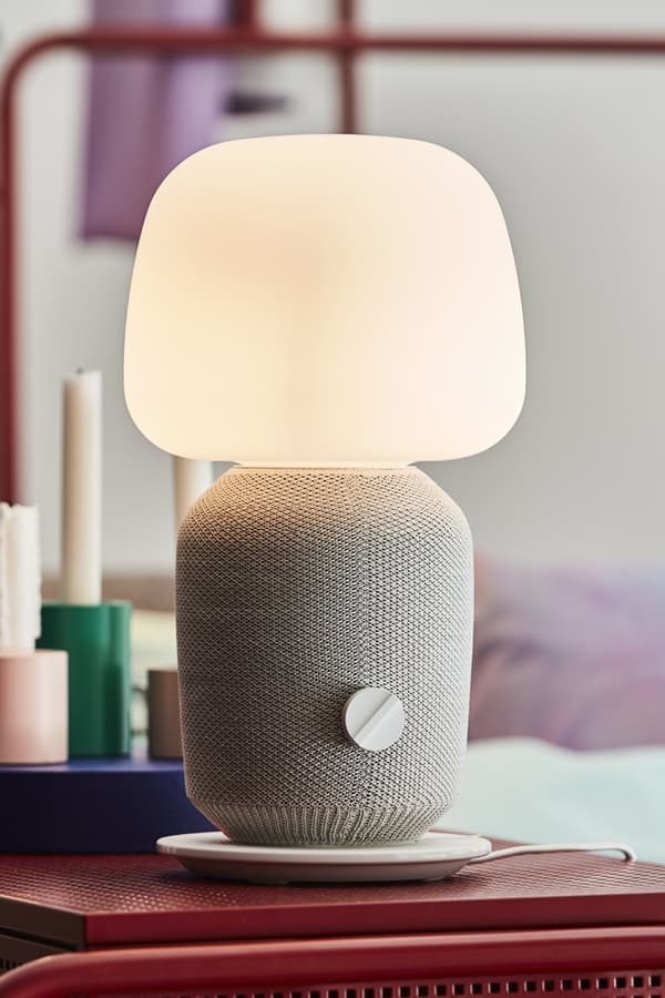 A white speaker lamp lit, sitting on a red table.