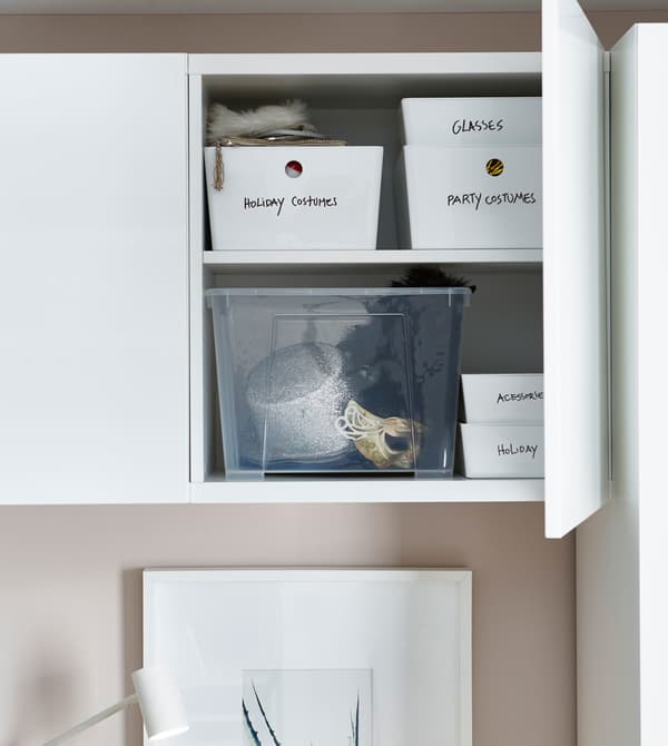 A white storage cabinet above a bed, opened to reveal labeled storage boxes within.