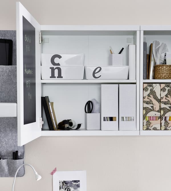 A white storage cabinet above a desk, opened to reveal labeled storage boxes within and white folder organisers inside.