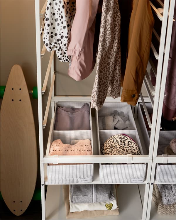 A white storage system, and at the bottom are STUK white and grey boxes with compartments where clothes are organised.