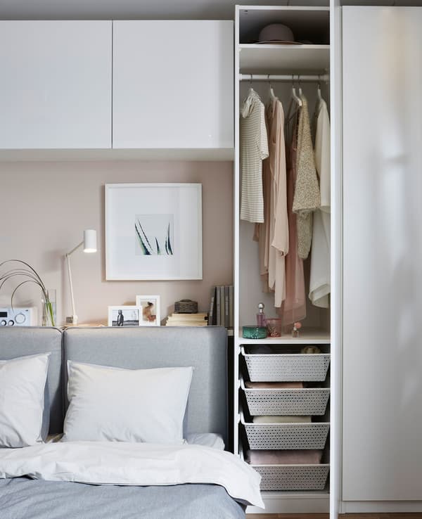 A white storage unit being used as a closet, with a clothes rail and four netted drawers to store clothes and accessories.