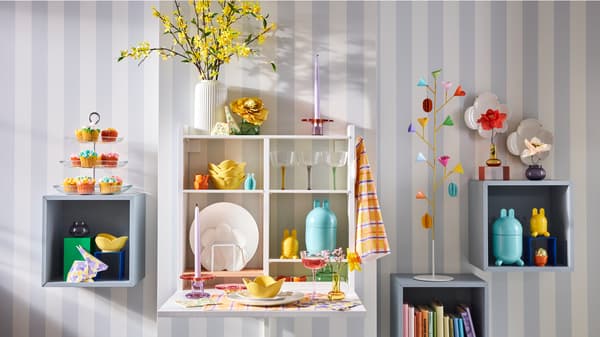 A white storage unit with shelves is attached to a wall. On the shelves, there are TJÄRLEK plates, bowls, egg cups, and more.