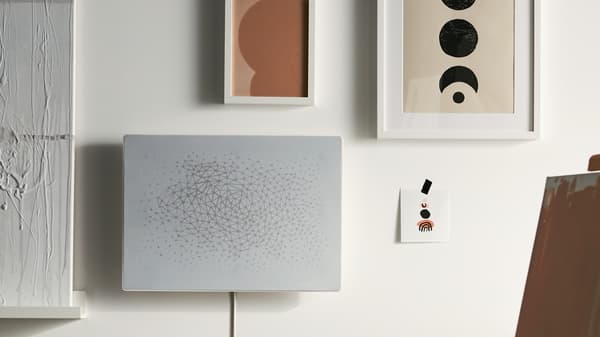 A white SYMFONISK picture frame with WiFi speaker on a white wall with two pictures in white frames above it.