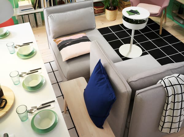 A white table, a bench and a grey sofa. The backside of the backrest is used as a backrest for the bench.