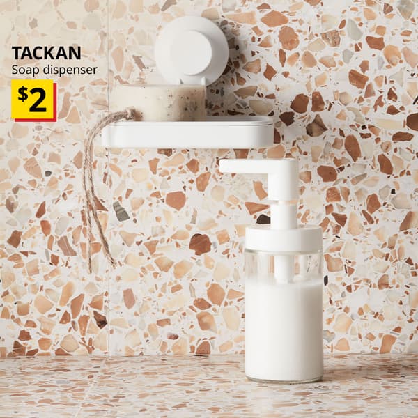 A white TACKAN soap dispenser placed on a brown-beige terrazo tiles featuring a white TISKEN soap dish with suction cup with a bar of soap on the wall. Black text on image reads "TACKAN, Soap dispenser. Price: $2" 