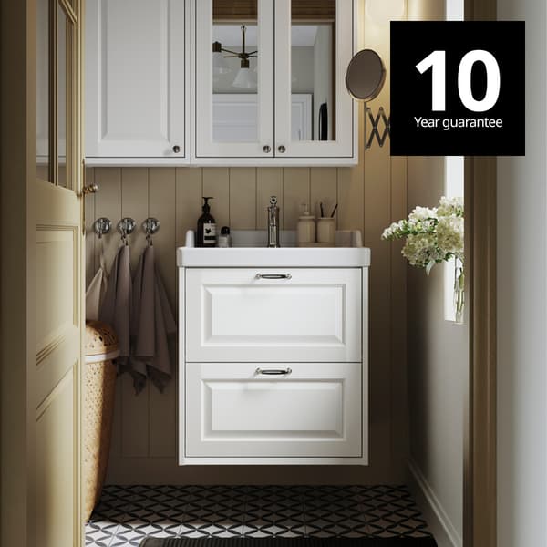 A white TÄNNFORSEN wash-stand with drawers and a matching mirror cabinet are placed in a bathroom with light brown walls. 10-year guarantee logo on top right corner.