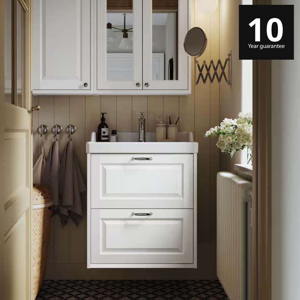 A white TÄNNFORSEN wash-stand with drawers and a matching mirror cabinet are placed in a bathroom with light brown walls. 10-year guarantee logo on top right corner.
