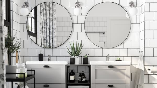 A white-tiled bathroom with two round mirrors, two washbasins in grey and white, a black trolley and three wall lamps.