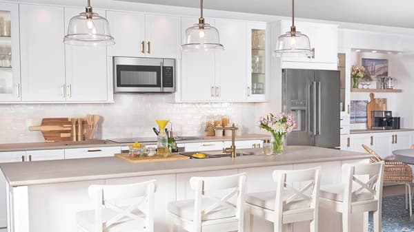 A white-tiled kitchen with matte white AXSTAD fronts and tall cabinets has black appliances and shelves on the wall.
