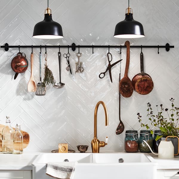 A white-tiled wall with a wall-mounted FINTORP rail with hooks. Herbs, kitchen utensils and decorative items hang here.