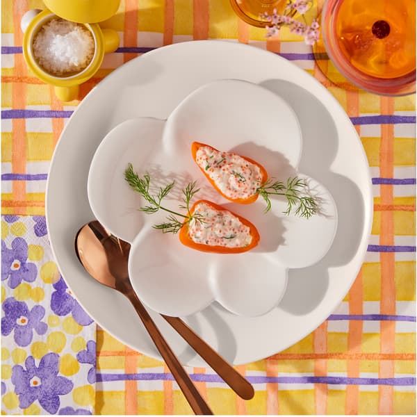 A white TJÄRLEK side plate is placed on a pink plate with cutlery on it. On the side plate, there is a small serving of food.