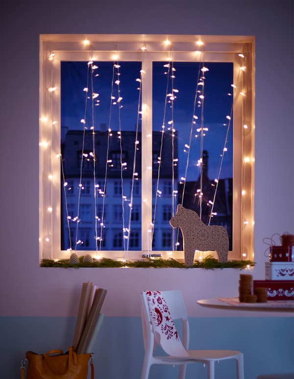 A white, tree-shaped candelabra sitting in a window with pomanders hanging above and pine cones lined up beside it.