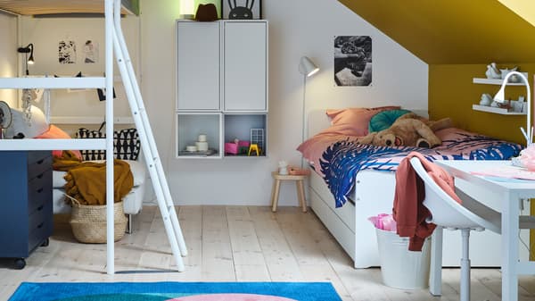 A white VITVAL loft bed stands opposite a white SLÄKT bed with underbed and storage in a children’s bedroom.
