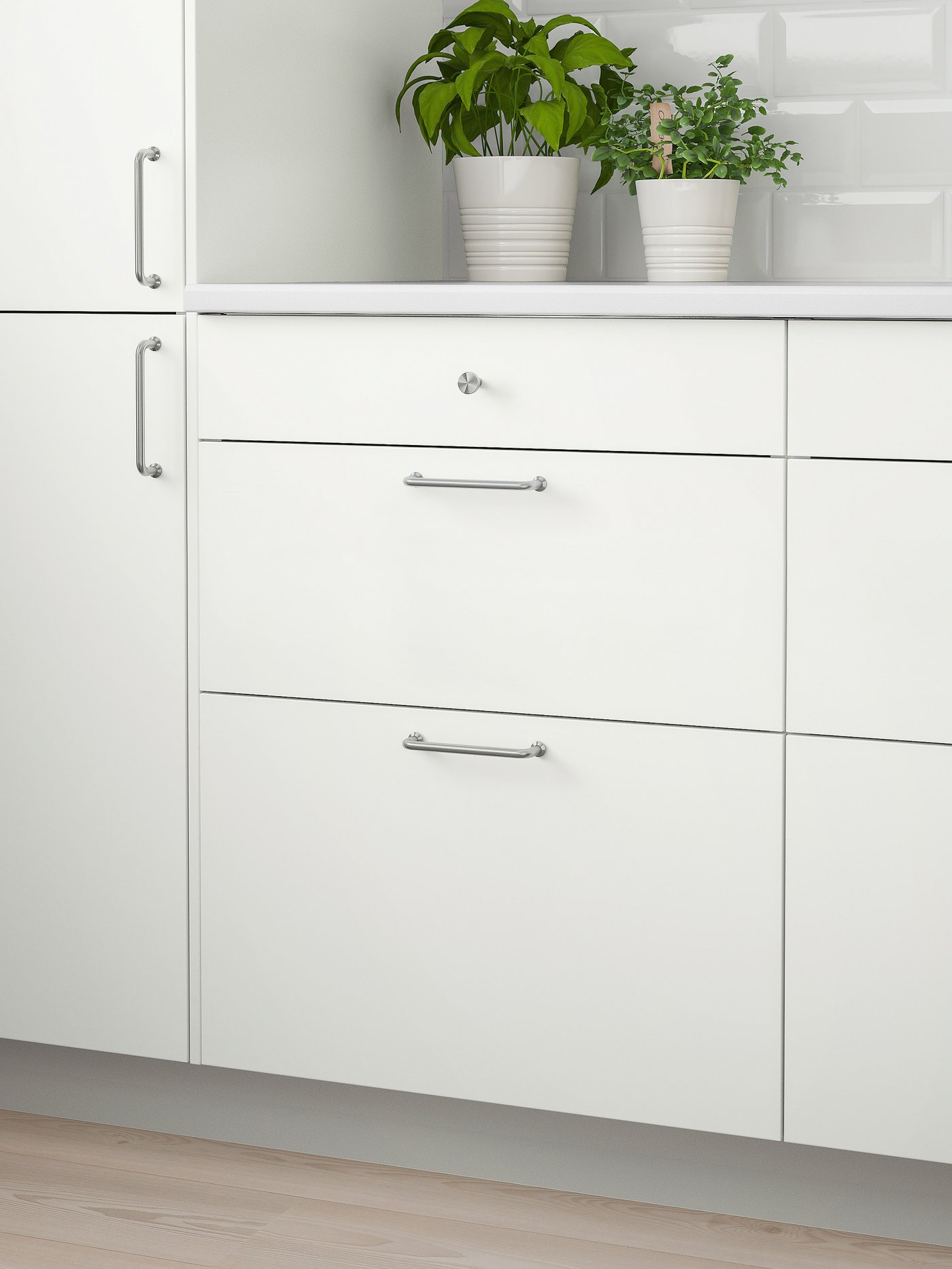 A white wall cabinet with two doors, a white worktop with two plants on top and three white drawers below.