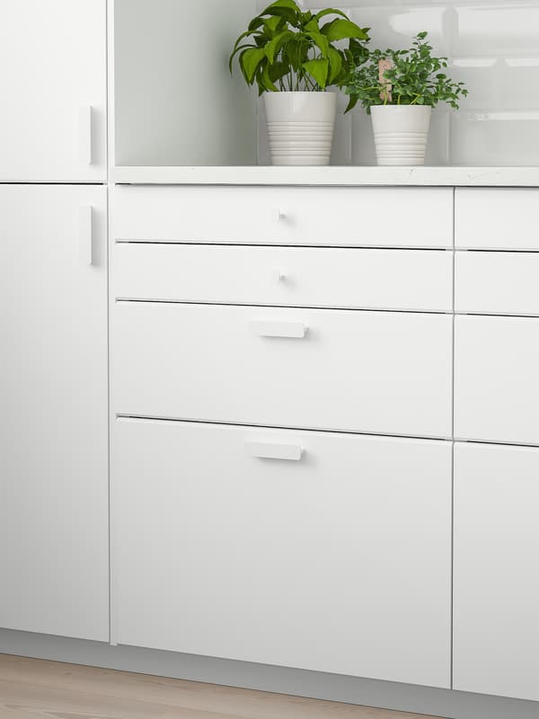 A white wall cabinet with two doors, a white worktop with two green plants on top and four white drawers below.