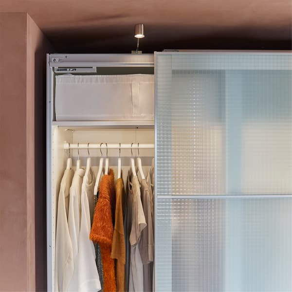 A white wardrobe with check pattern and frosted glass doors, cabinet lighting and white hangers.