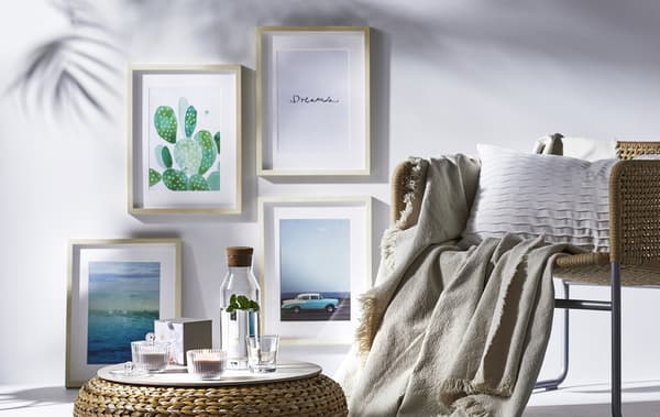 A wicker chair and footstool and artwork on a white wall.