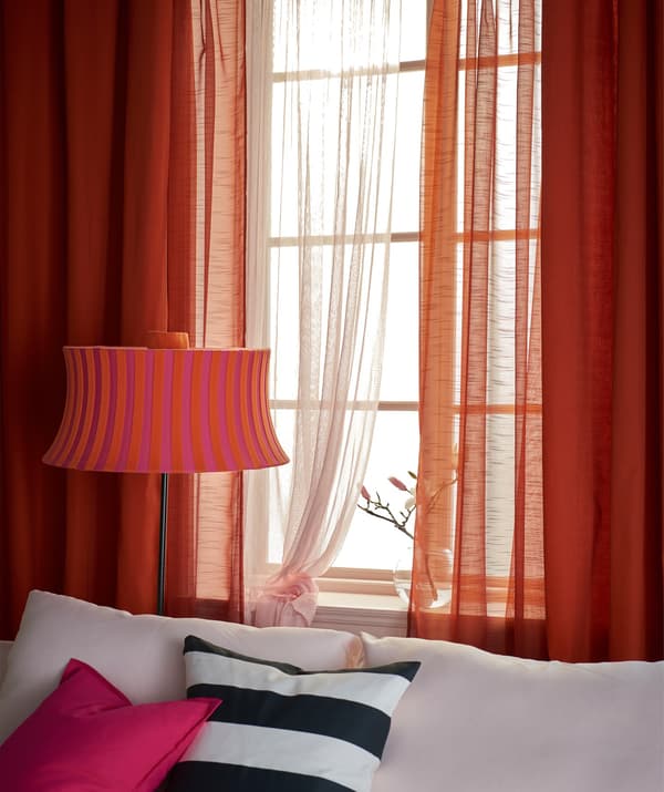 A window layered with orange and pink curtains, behind a sofa.