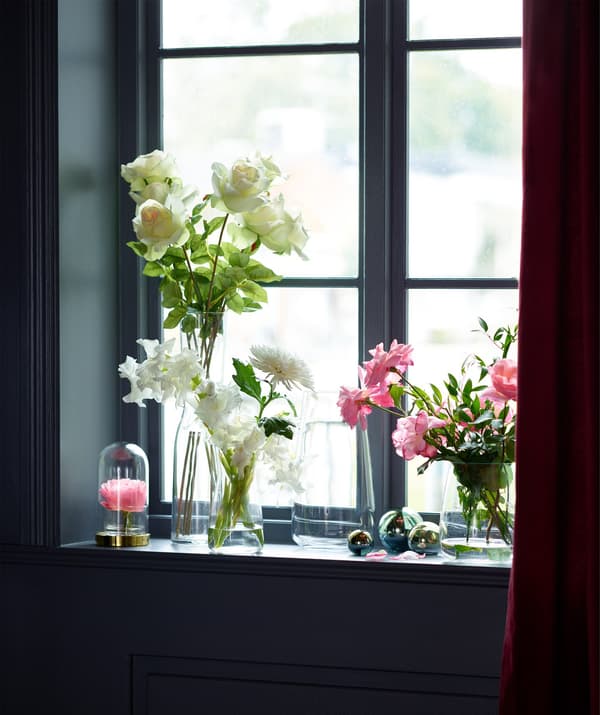 A window sill full of beautiful flower arrangements in BERÄKNA vases.