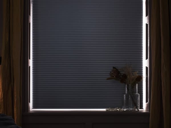 A window with a blackout shade pulled down and a tiny bit of light shining on the sides.