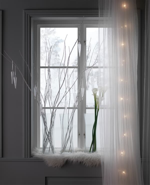 A window with a snowy view is decorate with glass vases, twigs and calla lilies.