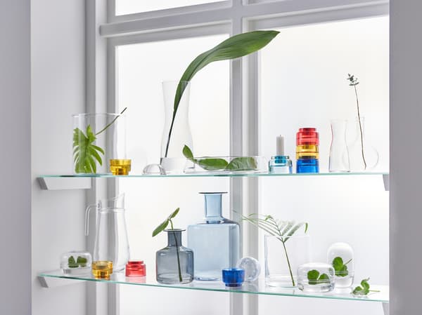 A window with light shining through it, and some glass shelves in the window containing glass bottles, jars and plants.