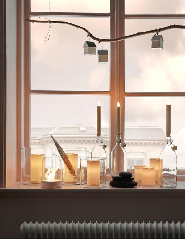 A windowsill decorated with natural hued LJUSANDE LED battery-operated candles and GODAFTON LED block candles.