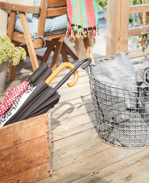 A wire basket with grey throws and a wooden box holding umbrellas.