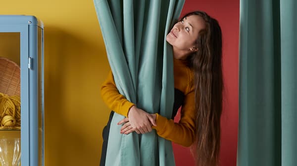 A woman against a yellow and red wall hugging a long teal curtain.