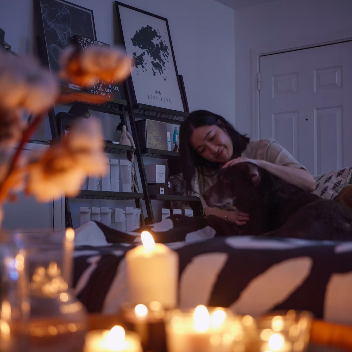 A woman and a dog relax in front of a table full of lit candles.