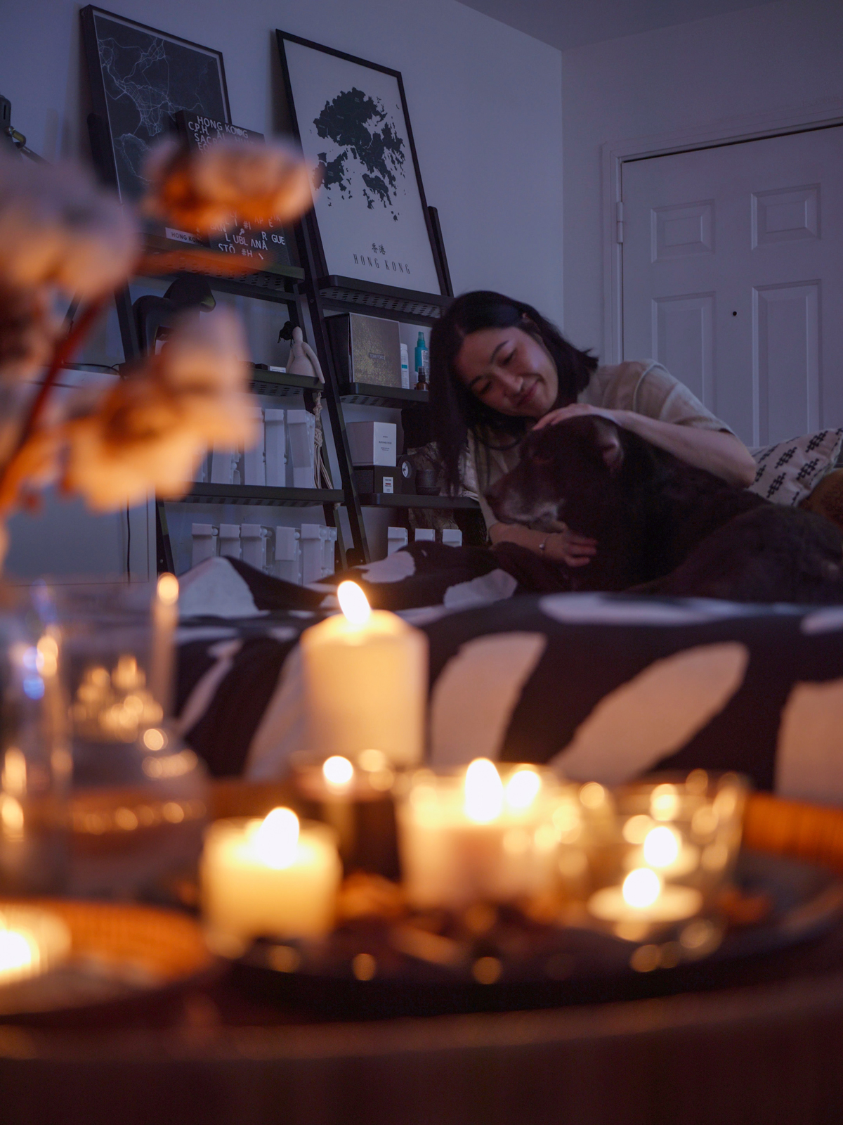 A woman and a dog relax in front of a table full of lit candles.