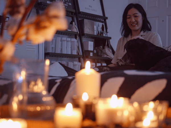 A woman and a dog relax in front of a table full of lit candles.