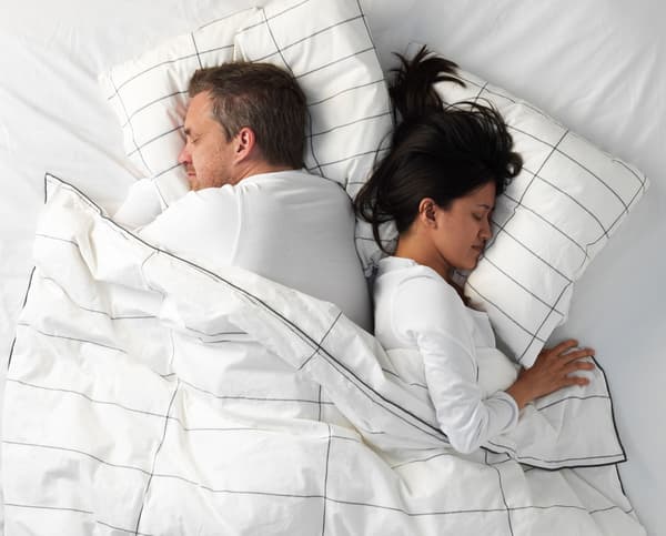 A woman and a man sleeping back to back under a striped duvet.