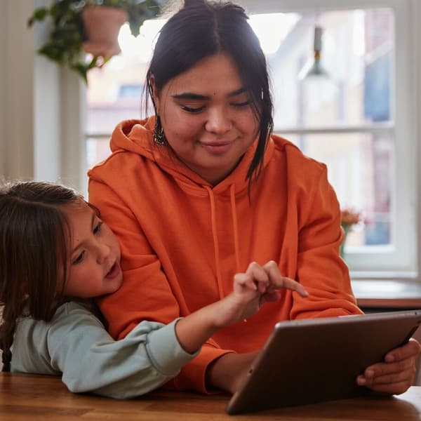 A woman and her child are sitting in the kitchen and looking at a tablet together.