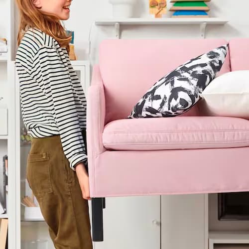 A woman carrying a pink sofa out of her living room.
