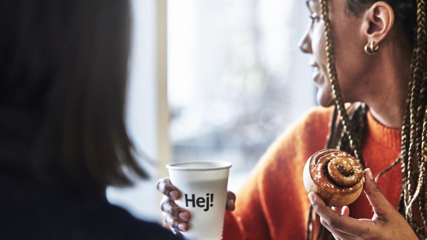 A woman drinks a cup of coffee and eating a cinnamon bun