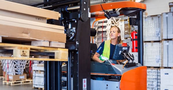A woman driving a forklift in a warehouse.