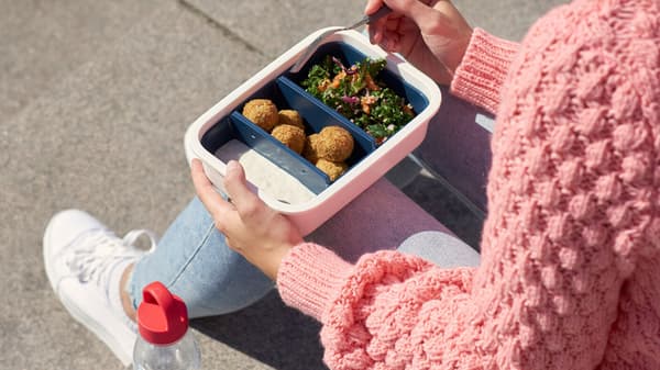 A woman eating from an IKEA plastic food container. 