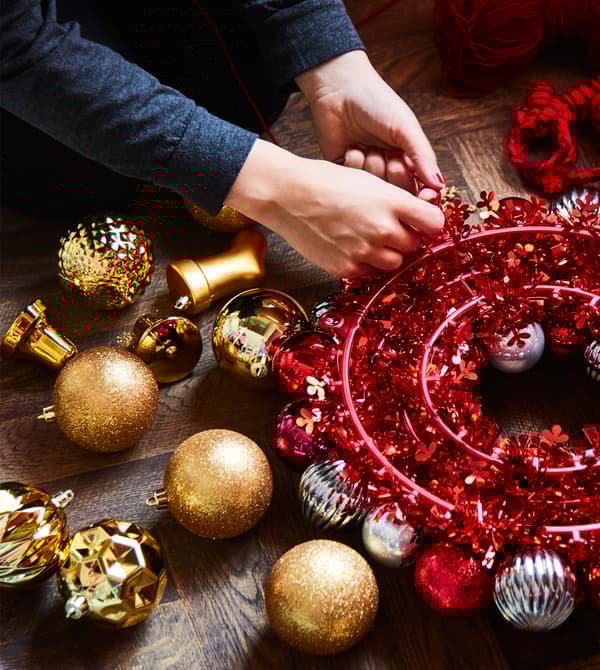 A woman fastens ornaments to a wreath to create a hanging centrepiece.