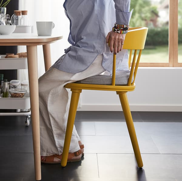 A woman gets up from the OMTÄNKSAM chair by holding on to the high back. The rounded back and seat add to the comfort.