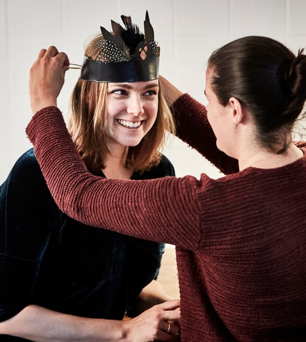 A woman helping another woman put on a harvest-themed head band.